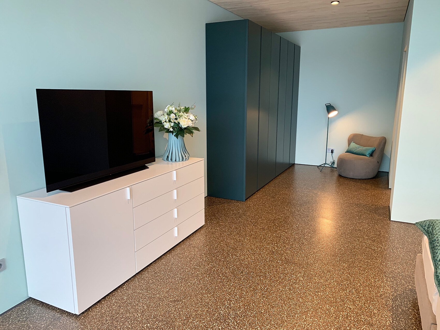 Modern living room: TV on white dresser, vase with flowers, blue walls, cabinets, reading lamp.