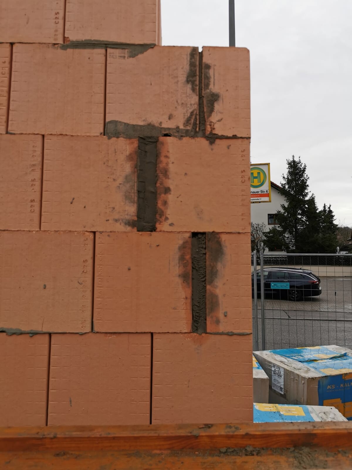 Ziegelwand mit dunkler Mörtelverfugung an einer Baustelle; Hintergrund Auto und Zaun erkennbar.
