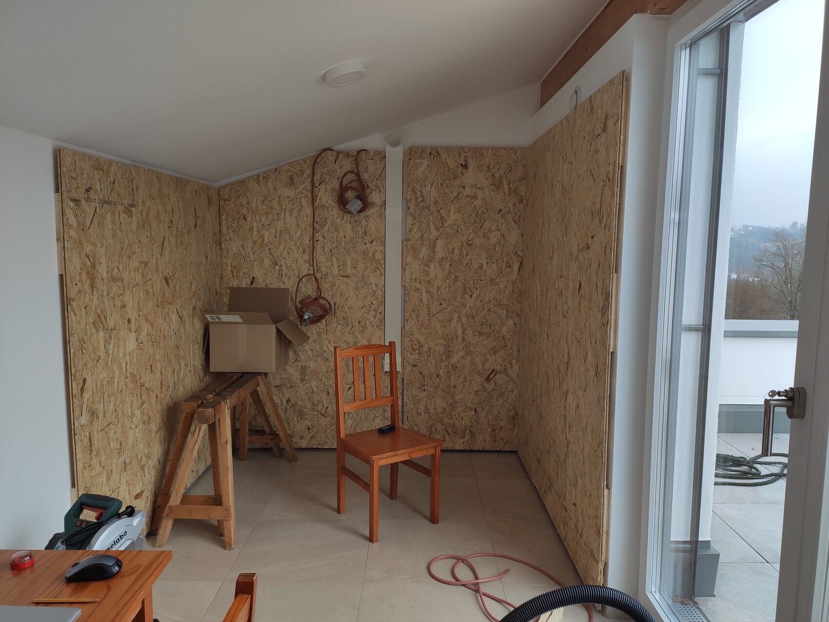 Renovation room with OSB walls, construction tools, wooden beams, and balcony access
