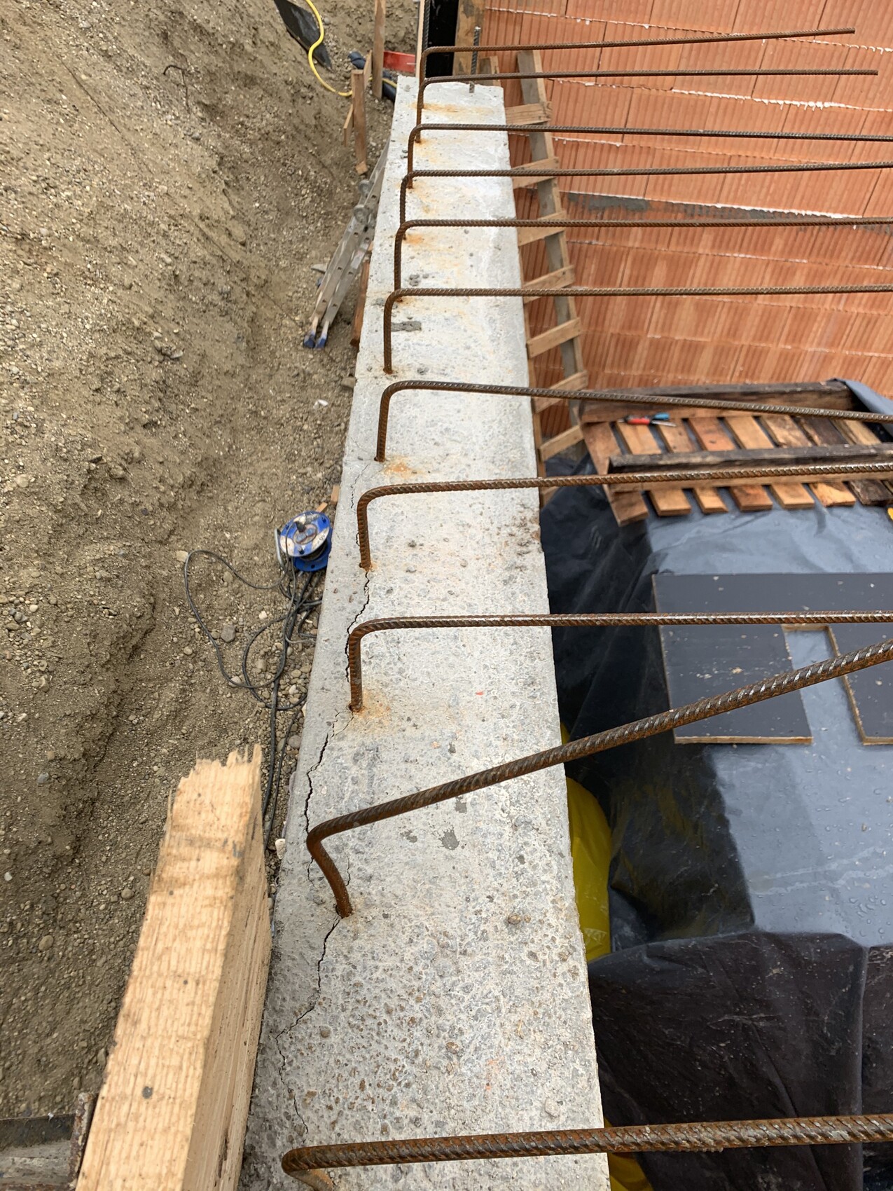 Rusty reinforcing bars protruding from a concrete edge; soil and wooden formwork nearby.