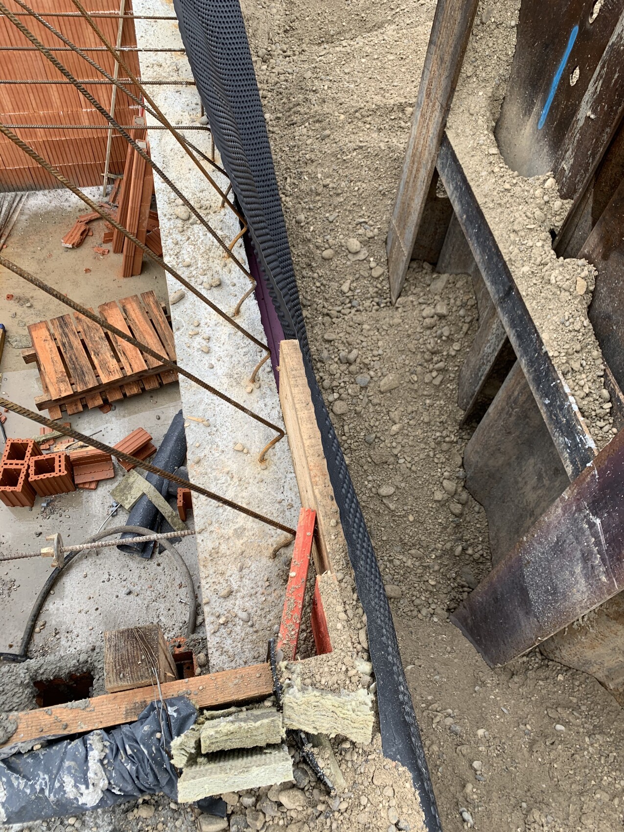 Construction site: foundation trench with reinforcing steel, bricks, wooden battens and soil.