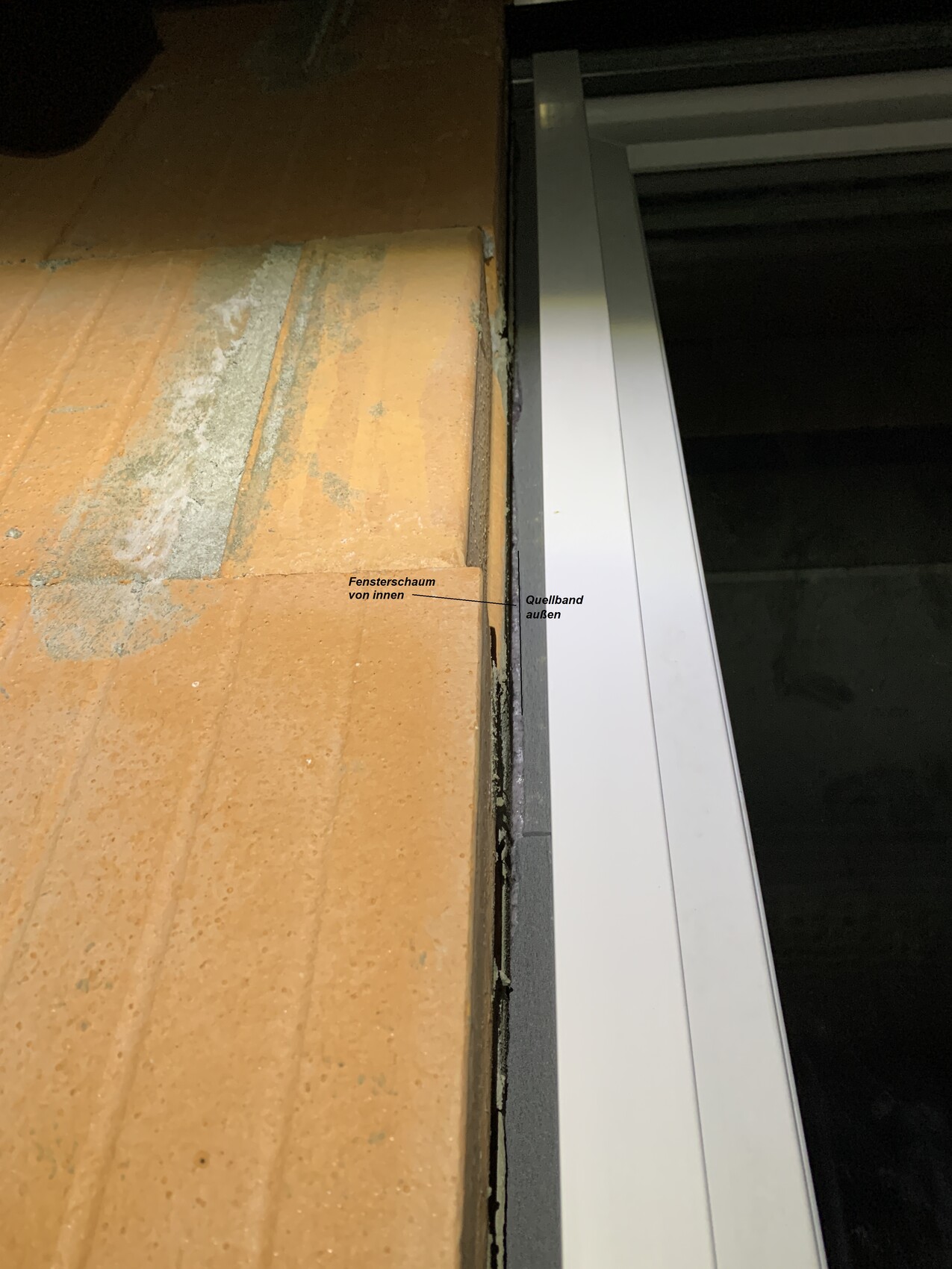 Window frame on brick wall; installation foam inside and swelling tape outside visible.