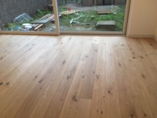 New wooden floor in the living room with a view outside through glass sliding doors.