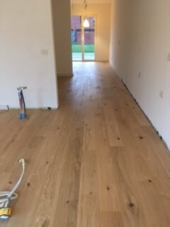 Empty interior with wooden floor, hallway leading to the door outside, construction phase.