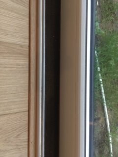 Close-up of a wooden window frame with glass, view outside to green area.