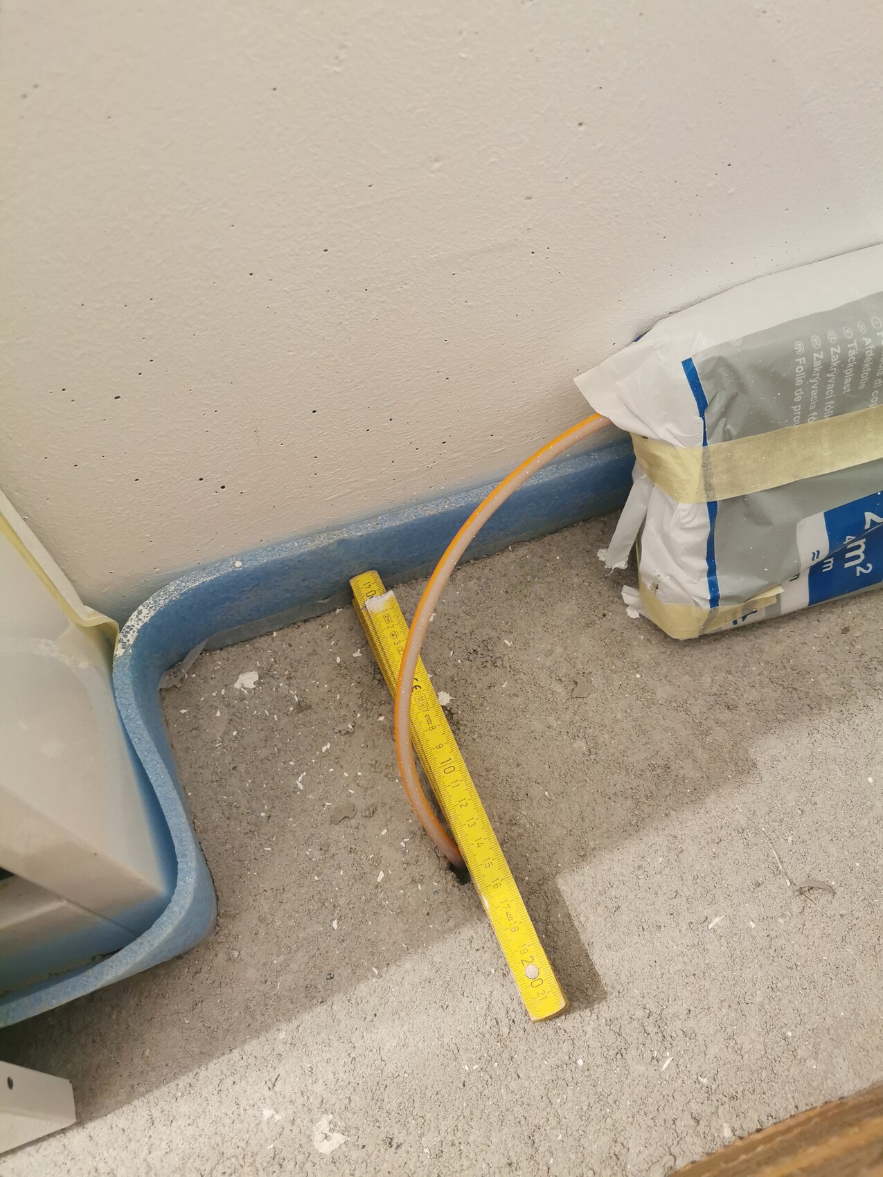 Construction site: open floor hole with measuring tape above, orange hose, construction material bag on the right.