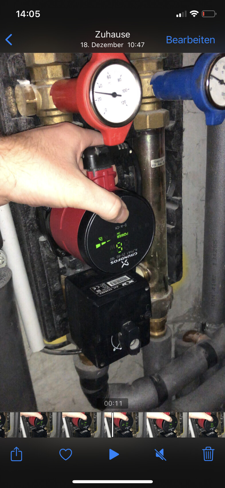 Close-up: hand turning red heating pump next to pressure gauge and pipes in heating system.