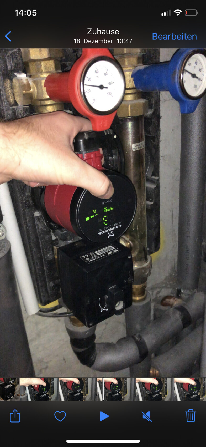 Person adjusting red pump control; visible pressure gauge and heating system pipes.