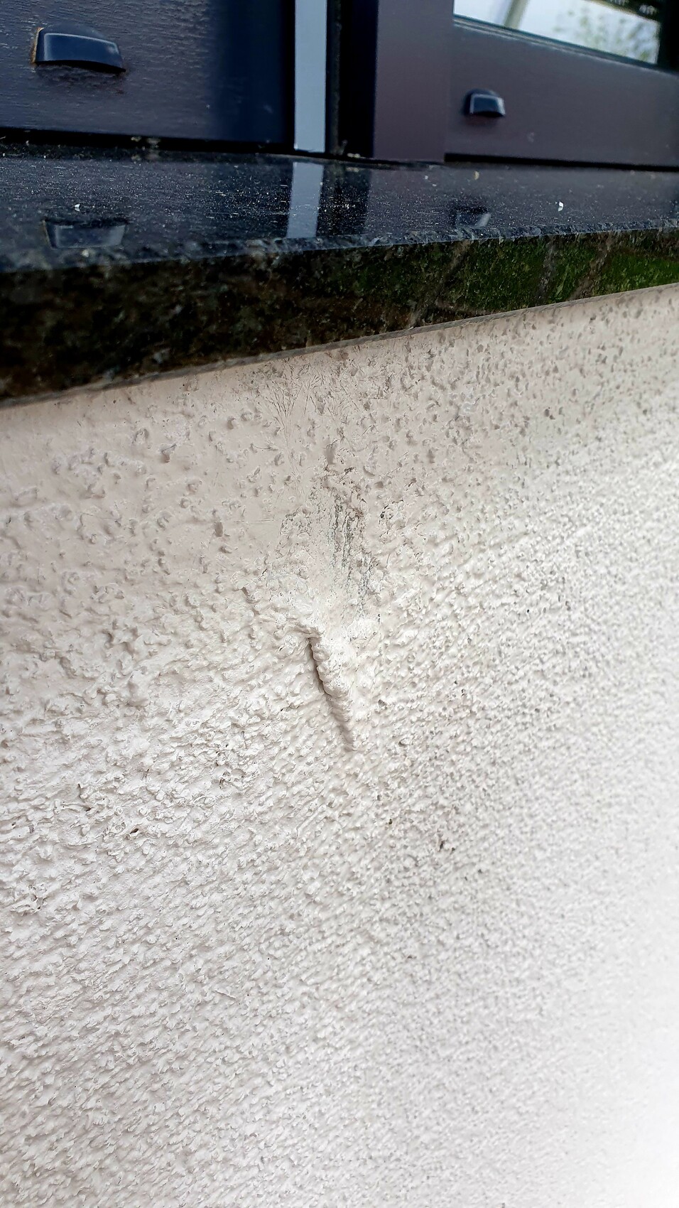 Exterior wall with rough render texture, vertical render crack below dark window sill.