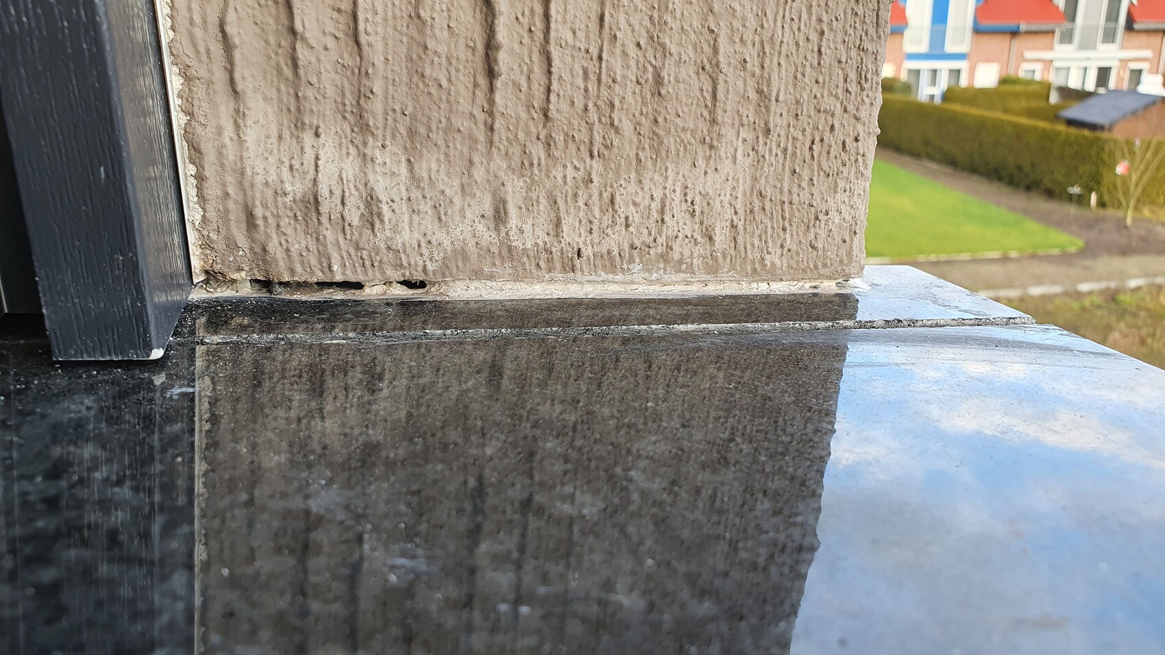 Close-up of a rough sandstone column on a black granite slab; background with houses.