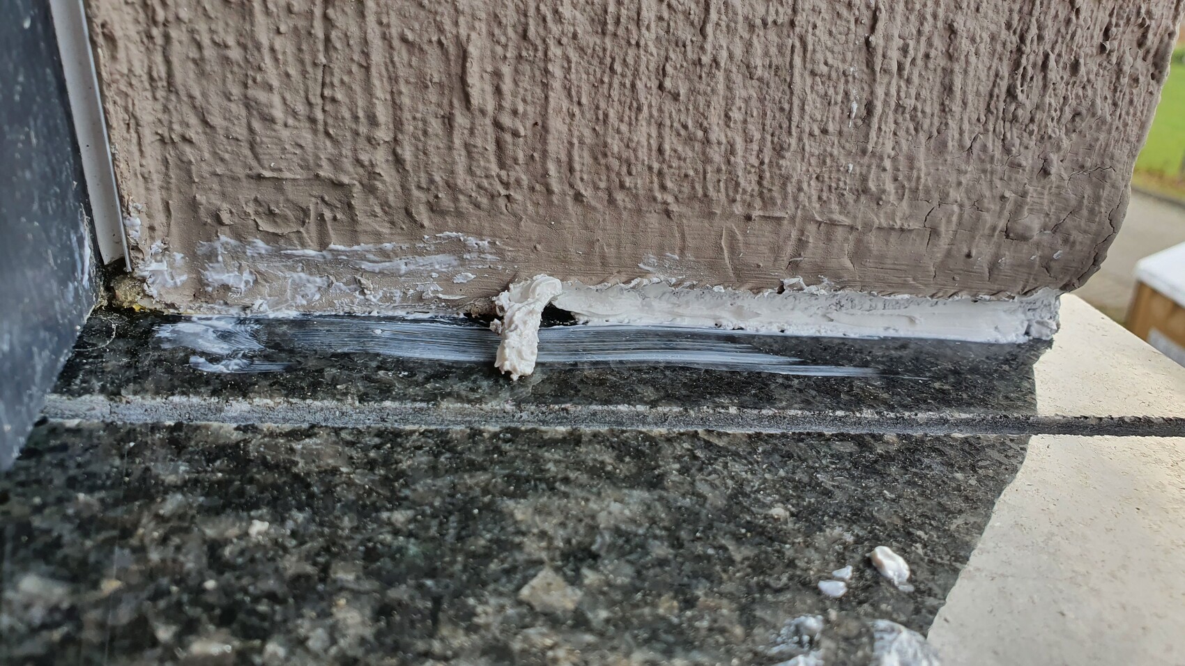 Close-up of a rough brown wall with white sealing compound in the joint above stone slab.