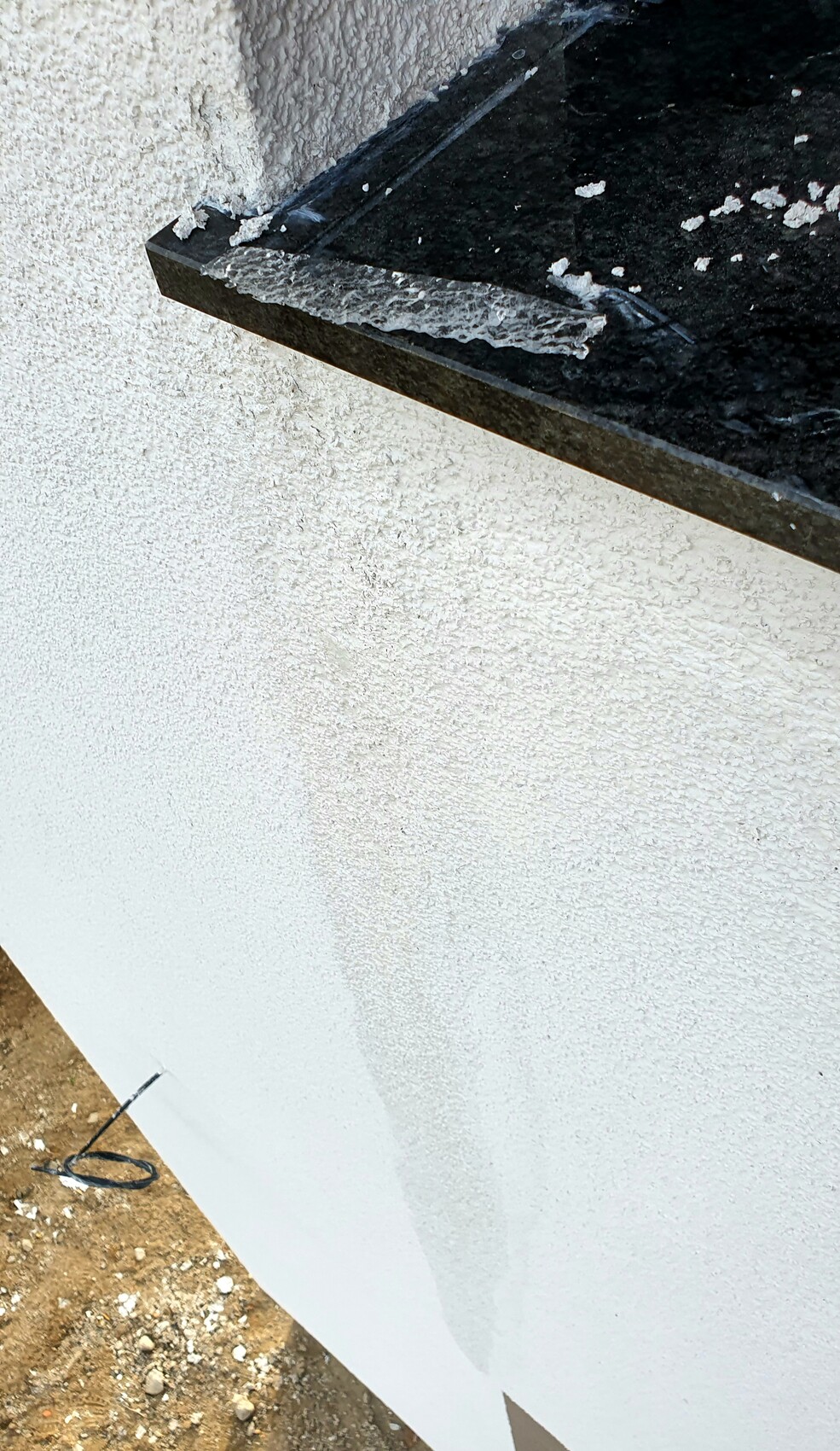 White rough wall with a black panel protruding from it and flaking edges.
