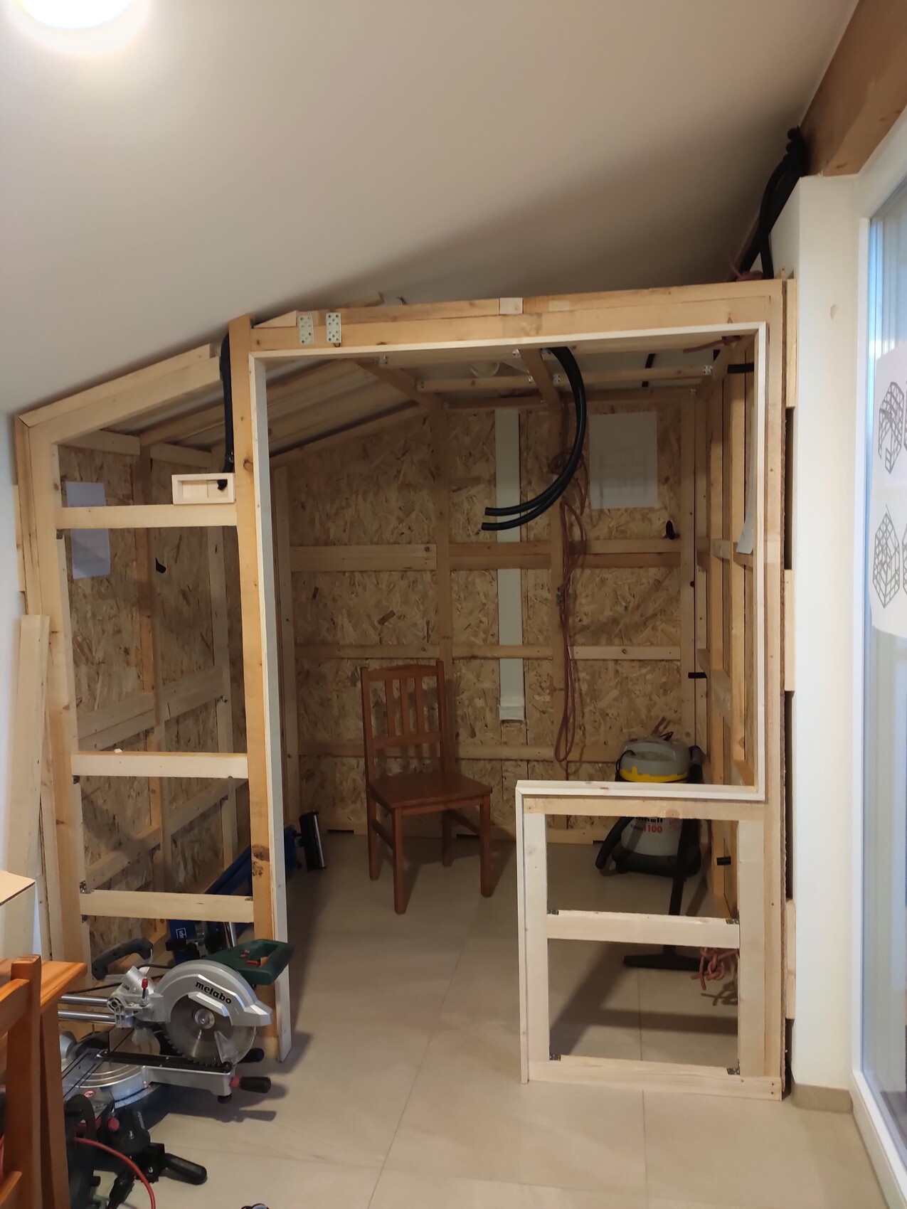 Unfinished interior with timber frame, OSB panels, chair and tools.