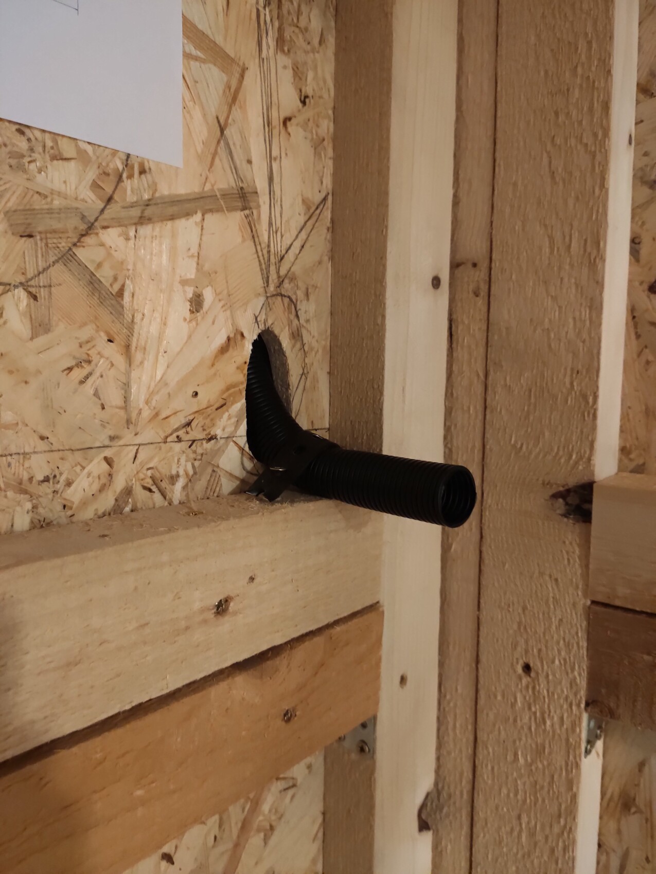 Black flexible conduit passing through a hole in an OSB wall of a timber construction.
