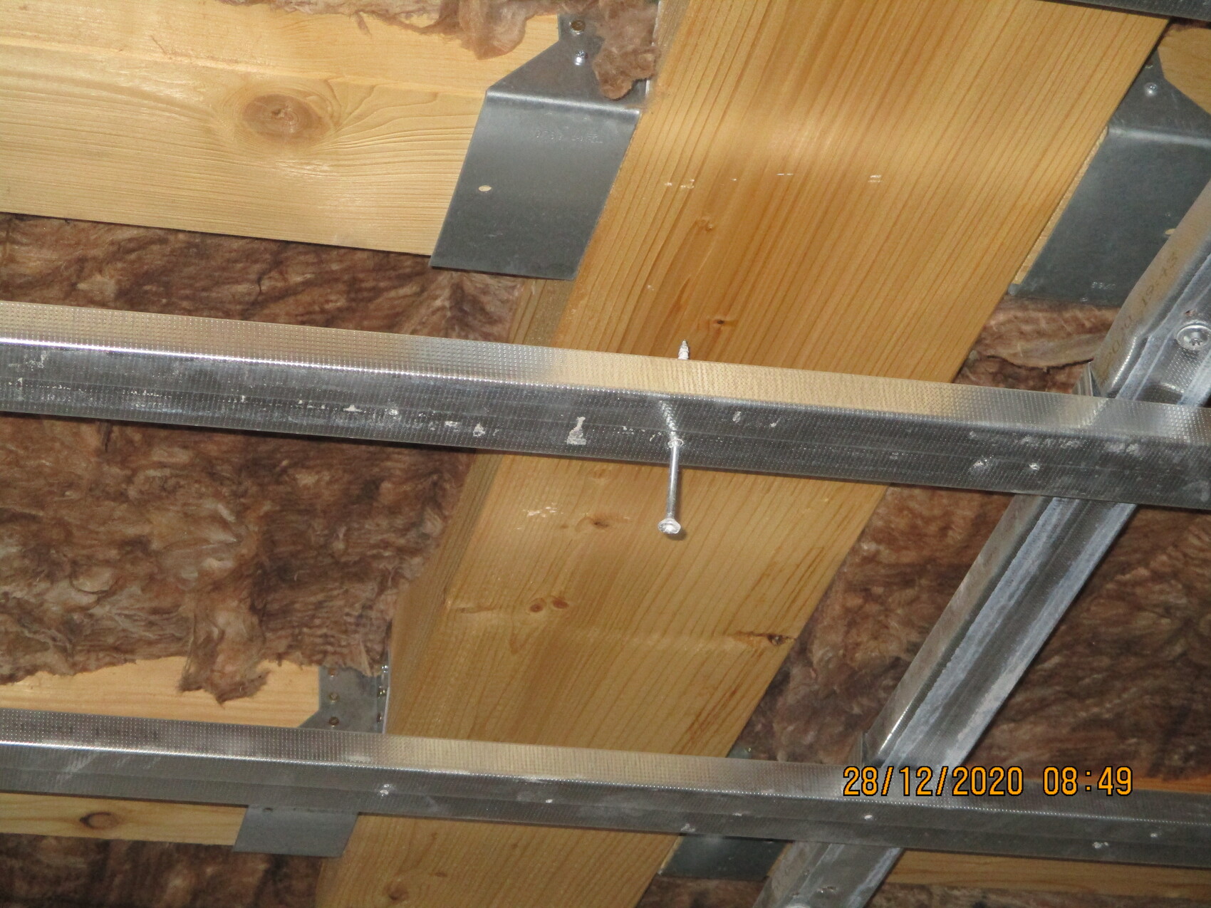 Dachbodenstruktur mit Holzbalken, brauner Dämmstoff, Metallträgern und Schraubbolzen.
