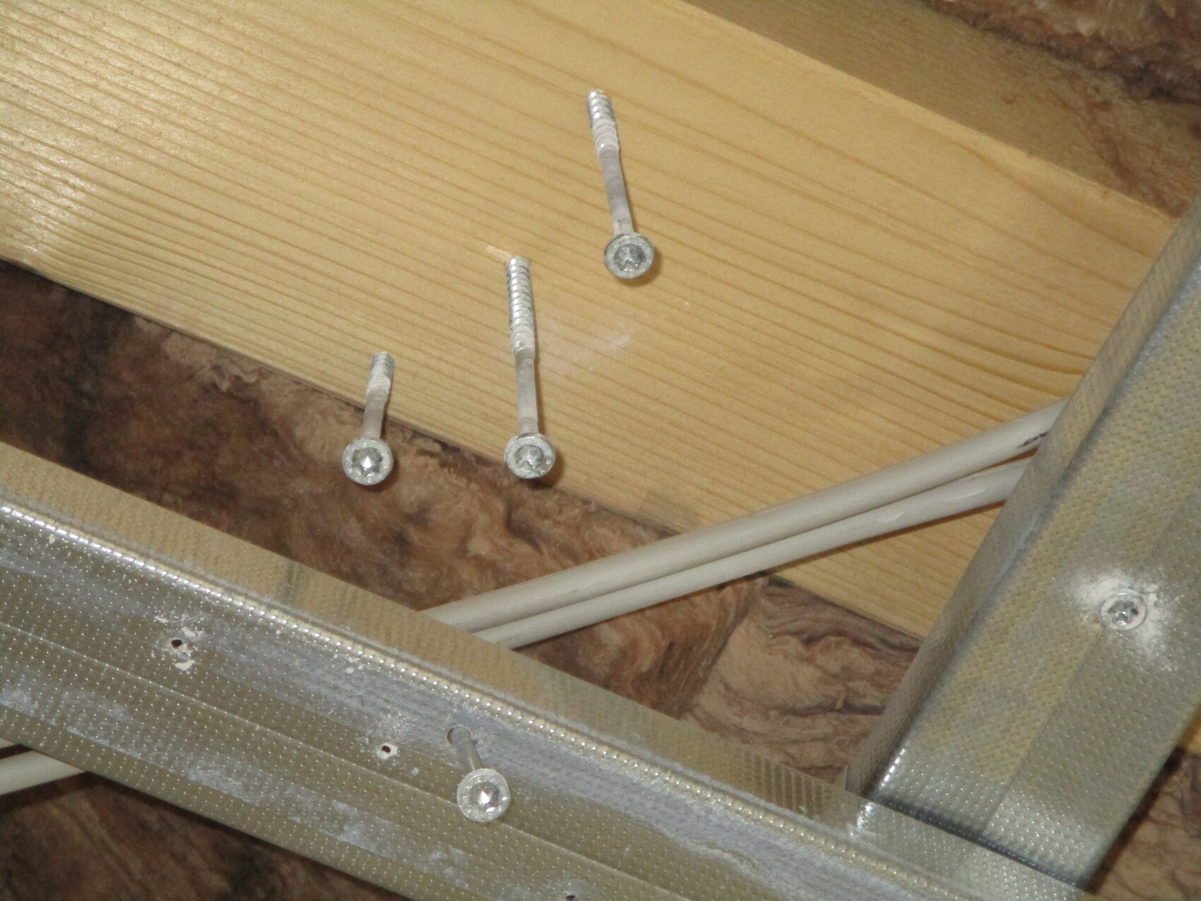 Holzbalken mit drei Schrauben, daneben weiße Kabel, darunter ein Metallprofil.