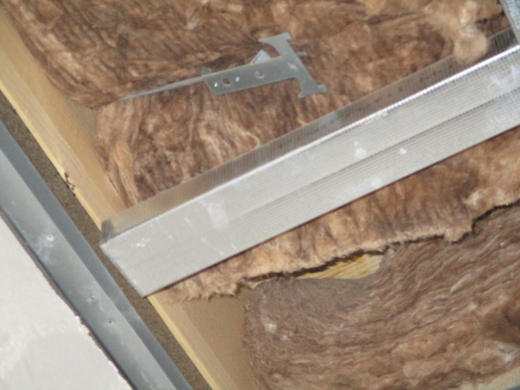 Dachboden: braune Dämmwolle, Holzlatten und silbernes Metallprofil.