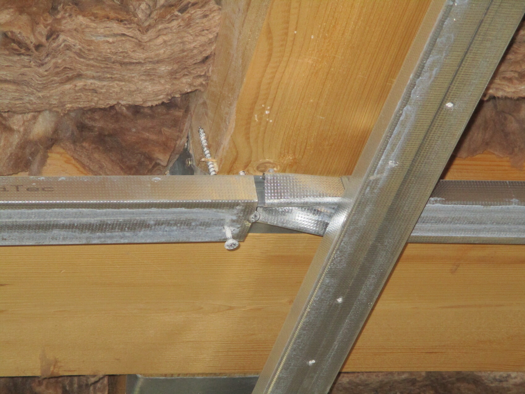 Dachbodenansicht: Silbere Metallträger kreuzen eine Holzdecke, dahinter Dämmmaterial.