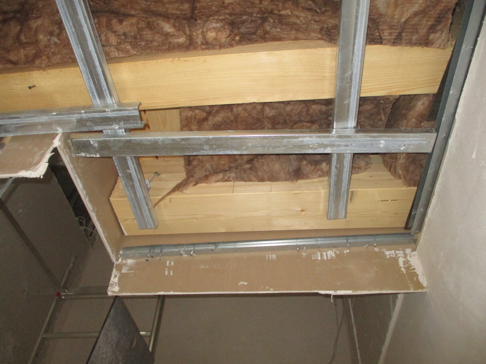 Durchgeschnittene Decke mit Metallprofilen, Holzlatten und brauner Dämmwolle sichtbar.