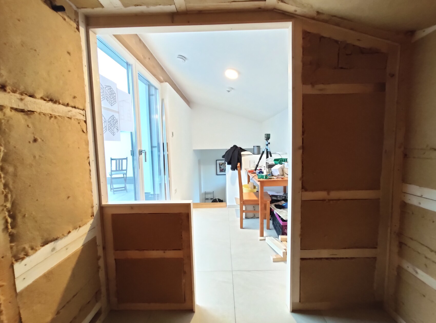 Shell construction view: door leads to bright interior with table, camera tripod, and tools.