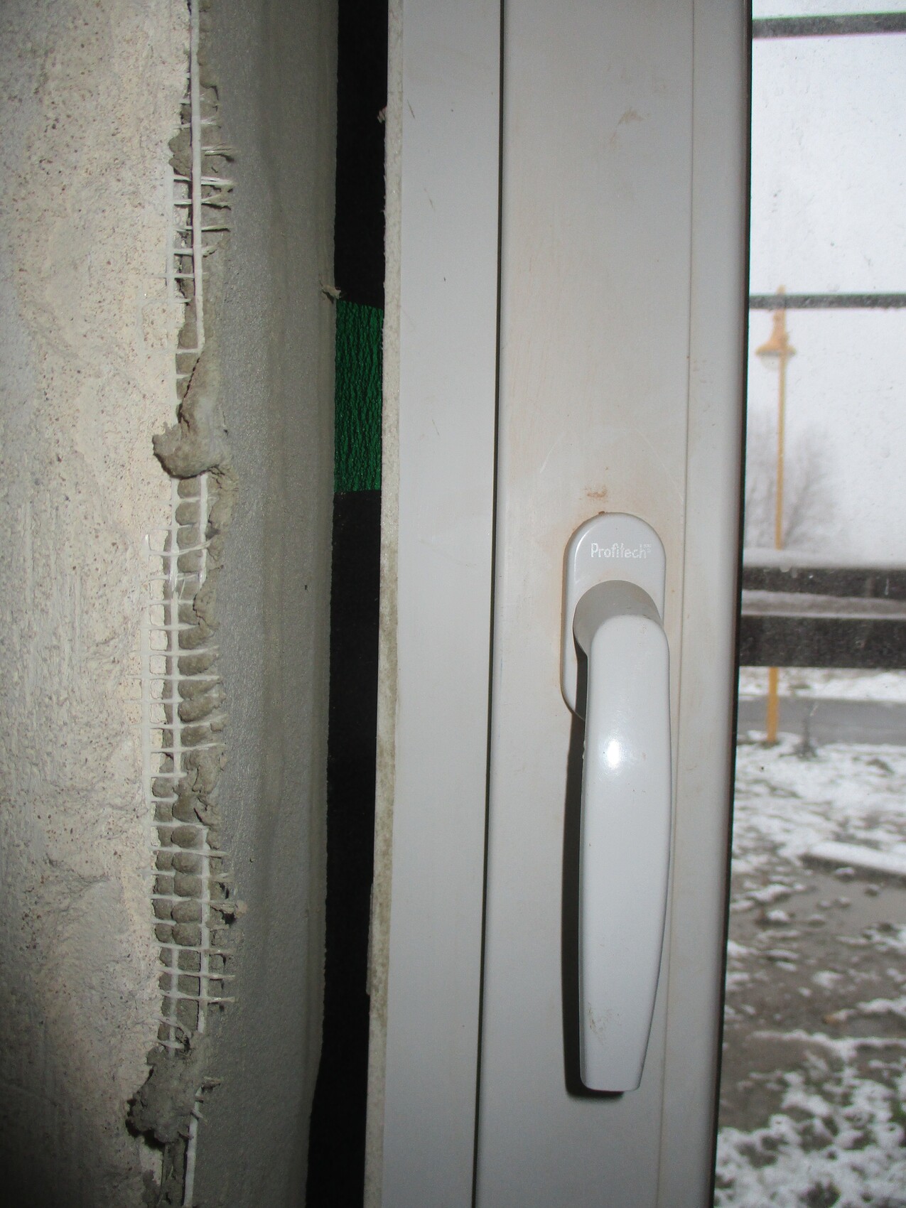 Close-up of a white window handle on the door frame; next to it, a wall with plaster damage.