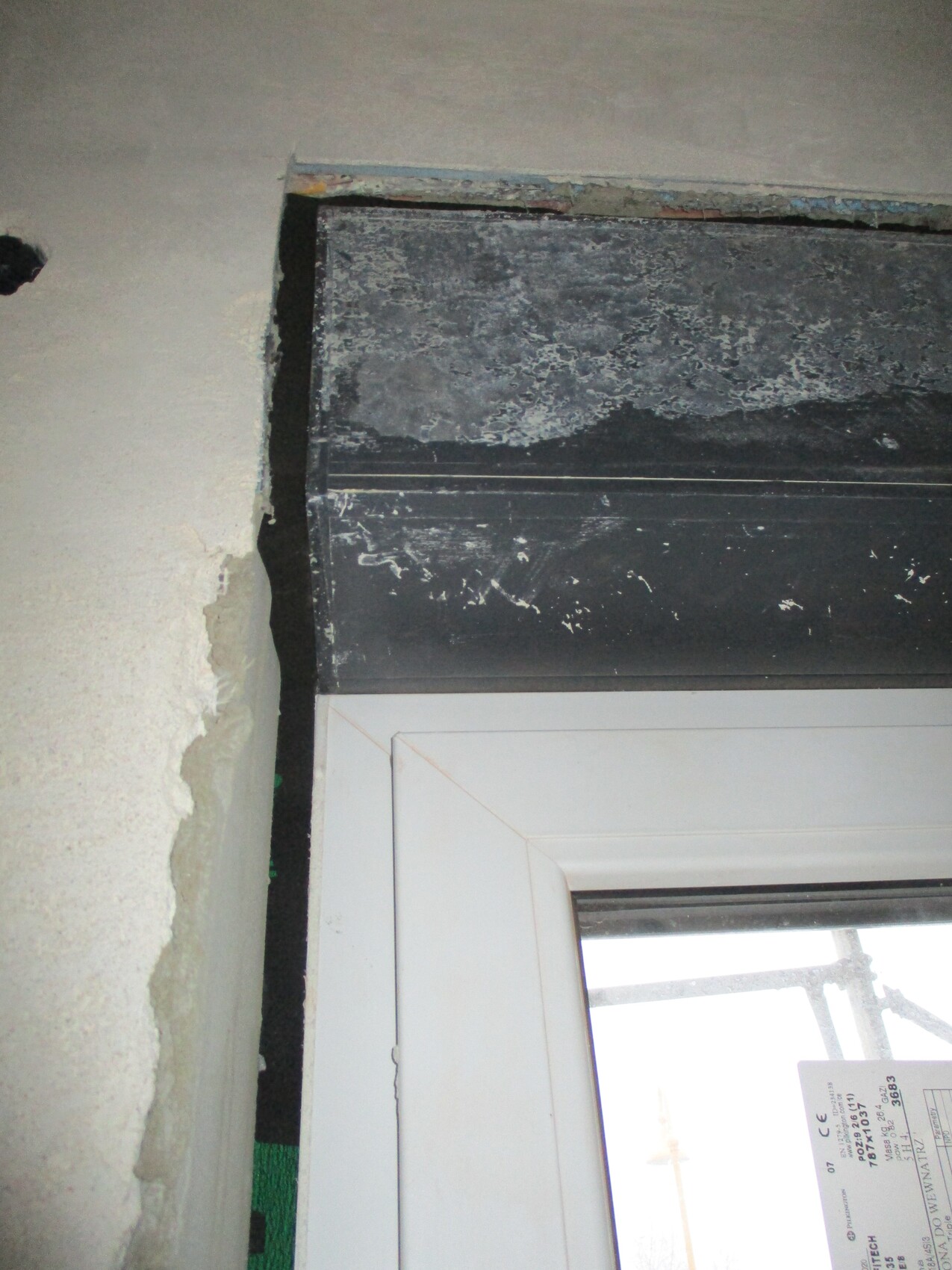 Shell construction: white window frame under black, dirty roller shutter guide; plaster crumbling.