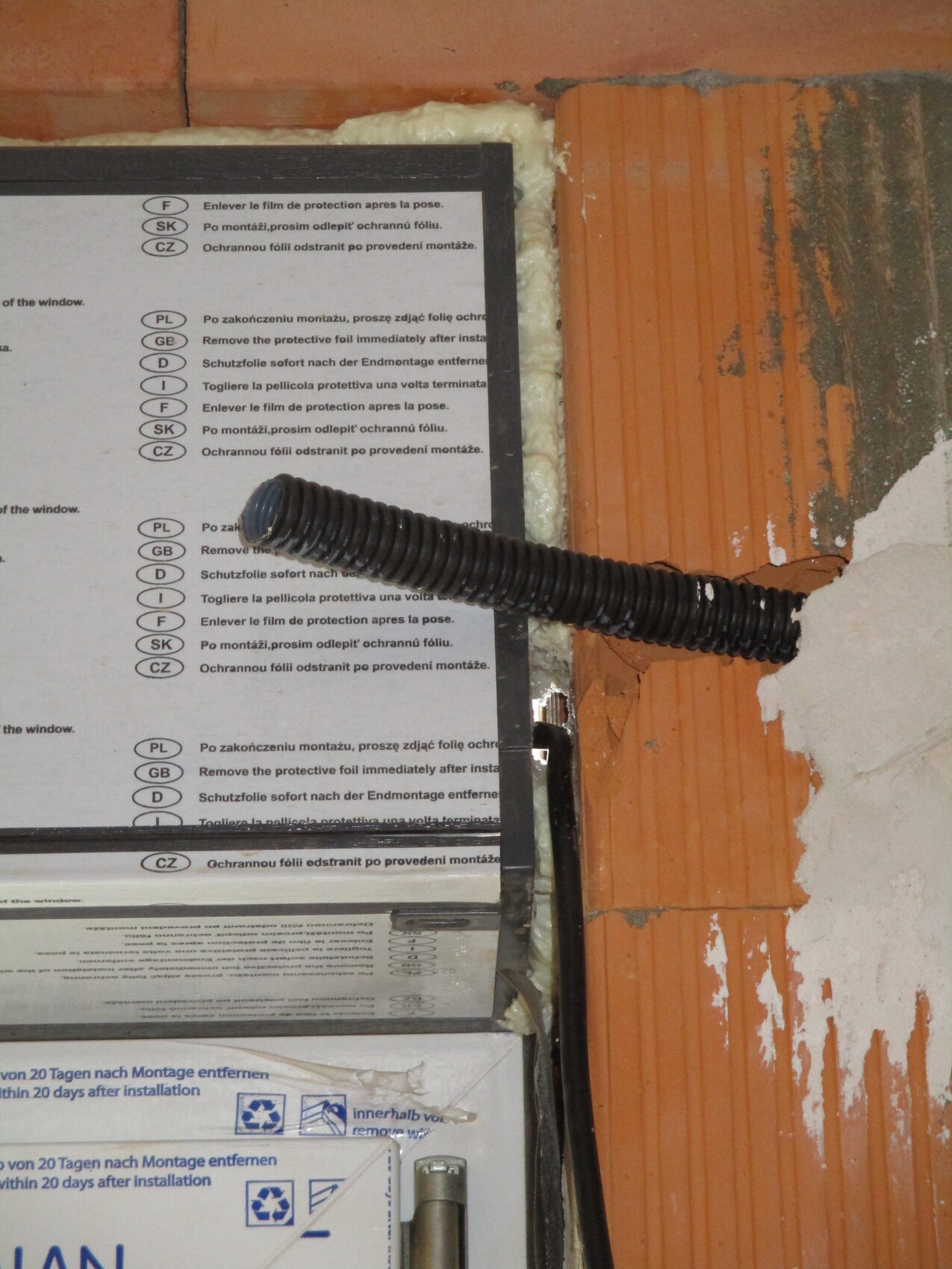 Black flexible conduit runs horizontally in front of an installation box on a brick wall.