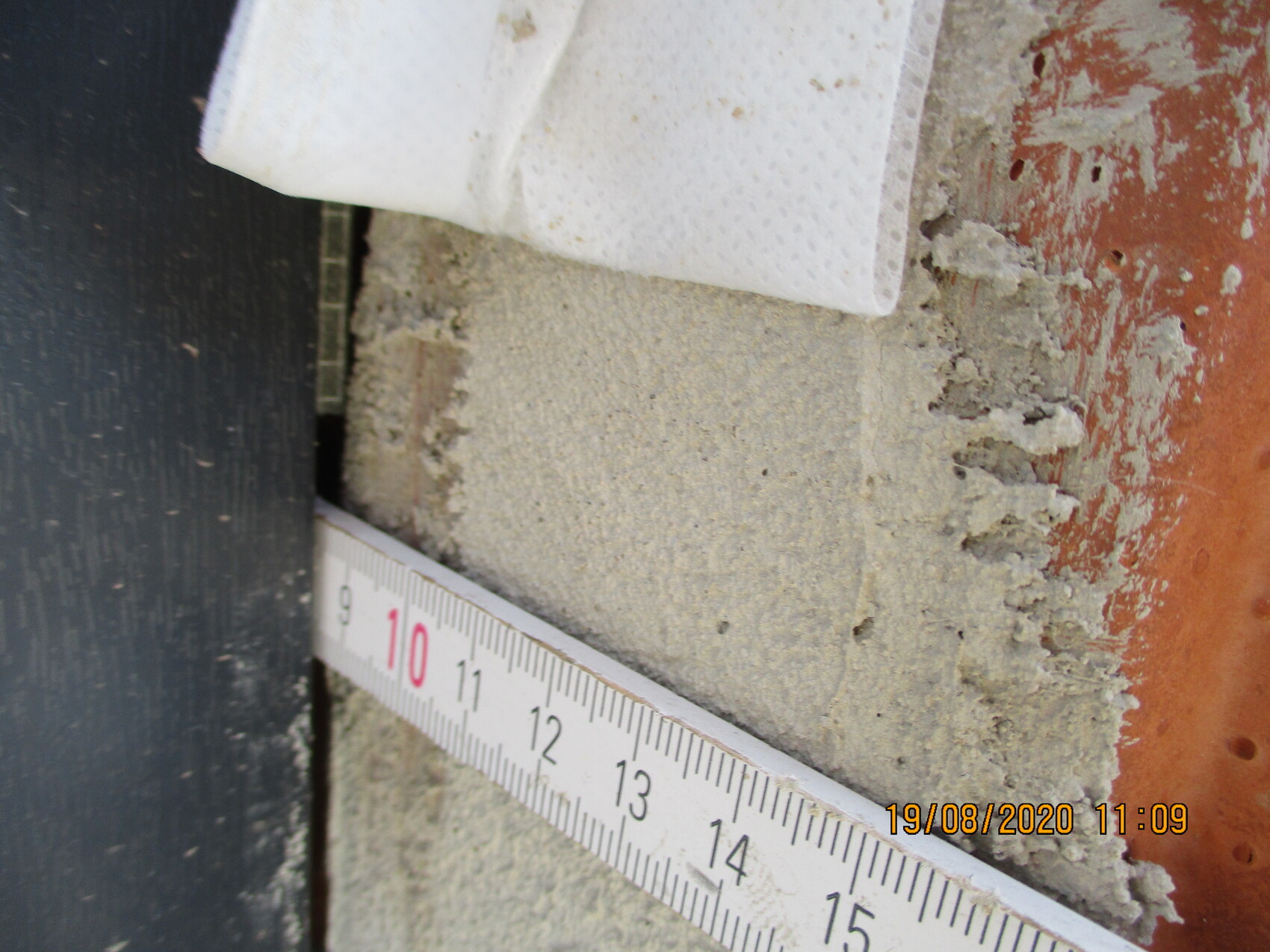 Close-up: Tape measure lying diagonally on rough concrete with brick and plaster debris.