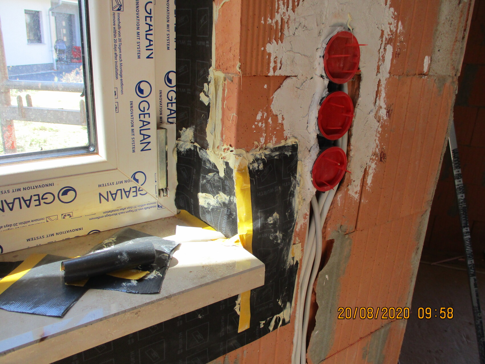 Construction site: interior wall made of brick with three red round pipe penetrations, cables and plaster residues.