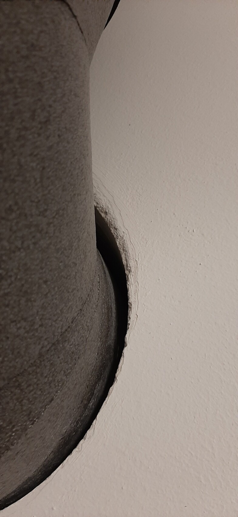 Close-up of a round hole in a wall with rough edges and a dark interior.