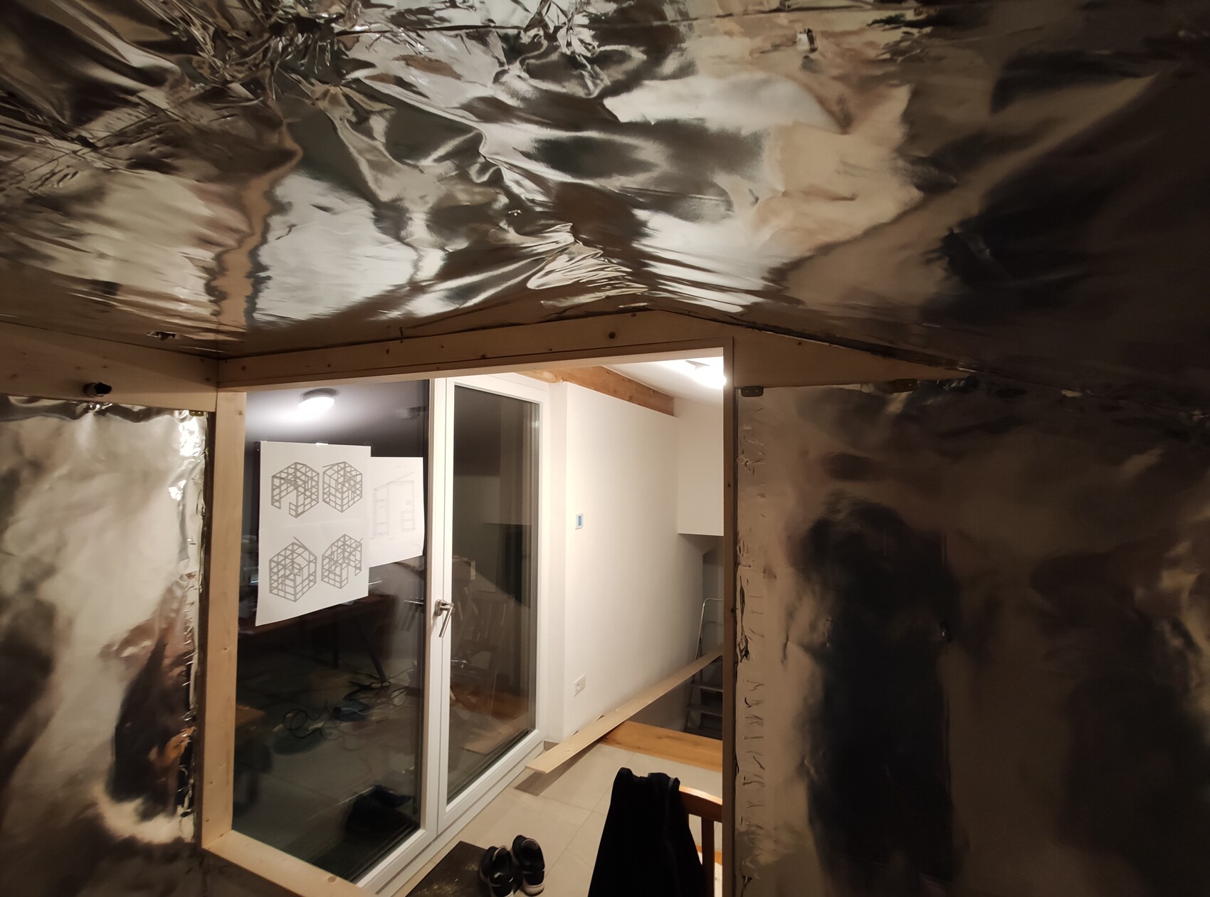 Renovated room: foil-covered ceiling, glass door, sketches on the glass, shoes on the floor.