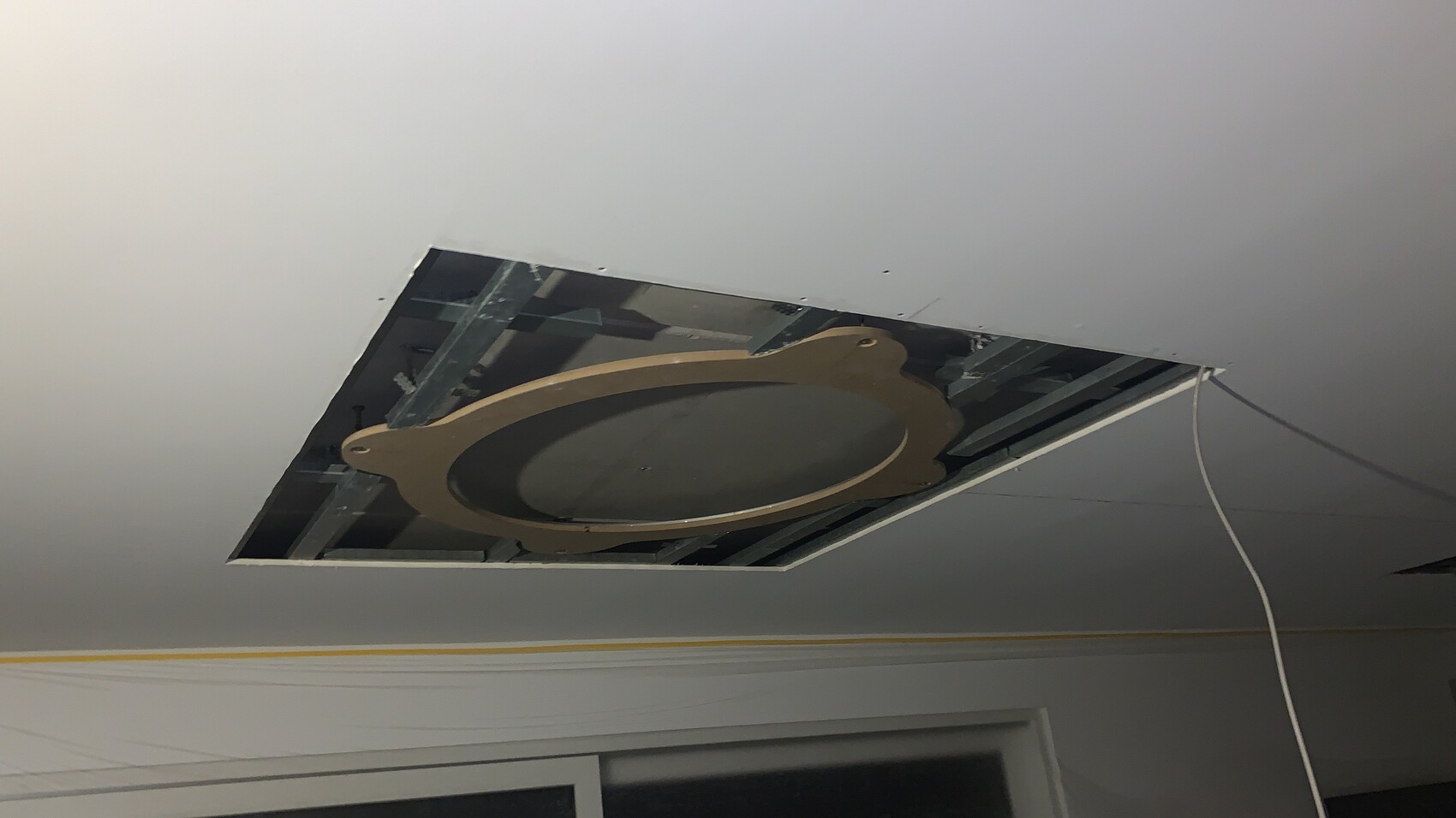 Ceiling opening with round beige ring, dark center; metal frame visible, cables hanging.