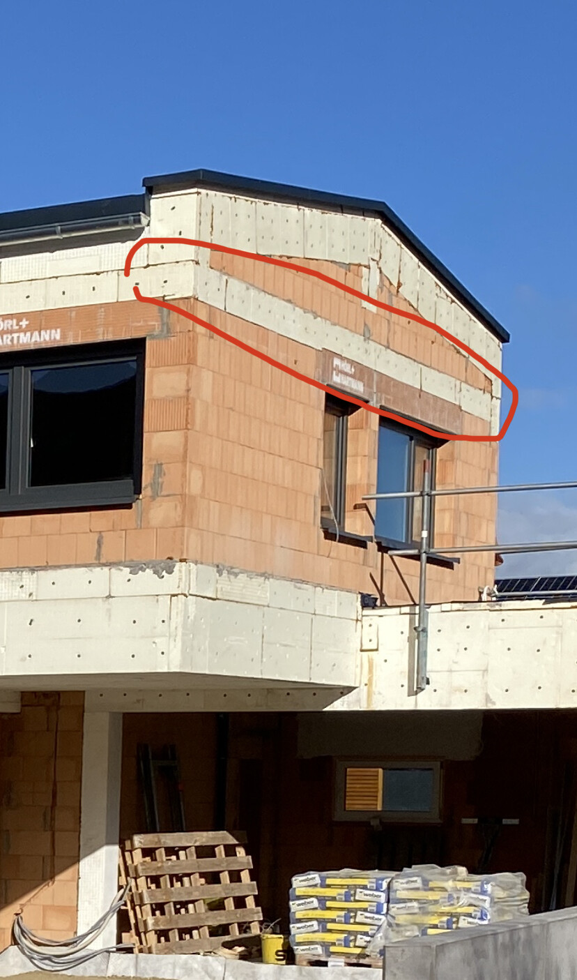Exterior view of a brick shell construction with windows, scaffolding, and pallets.
