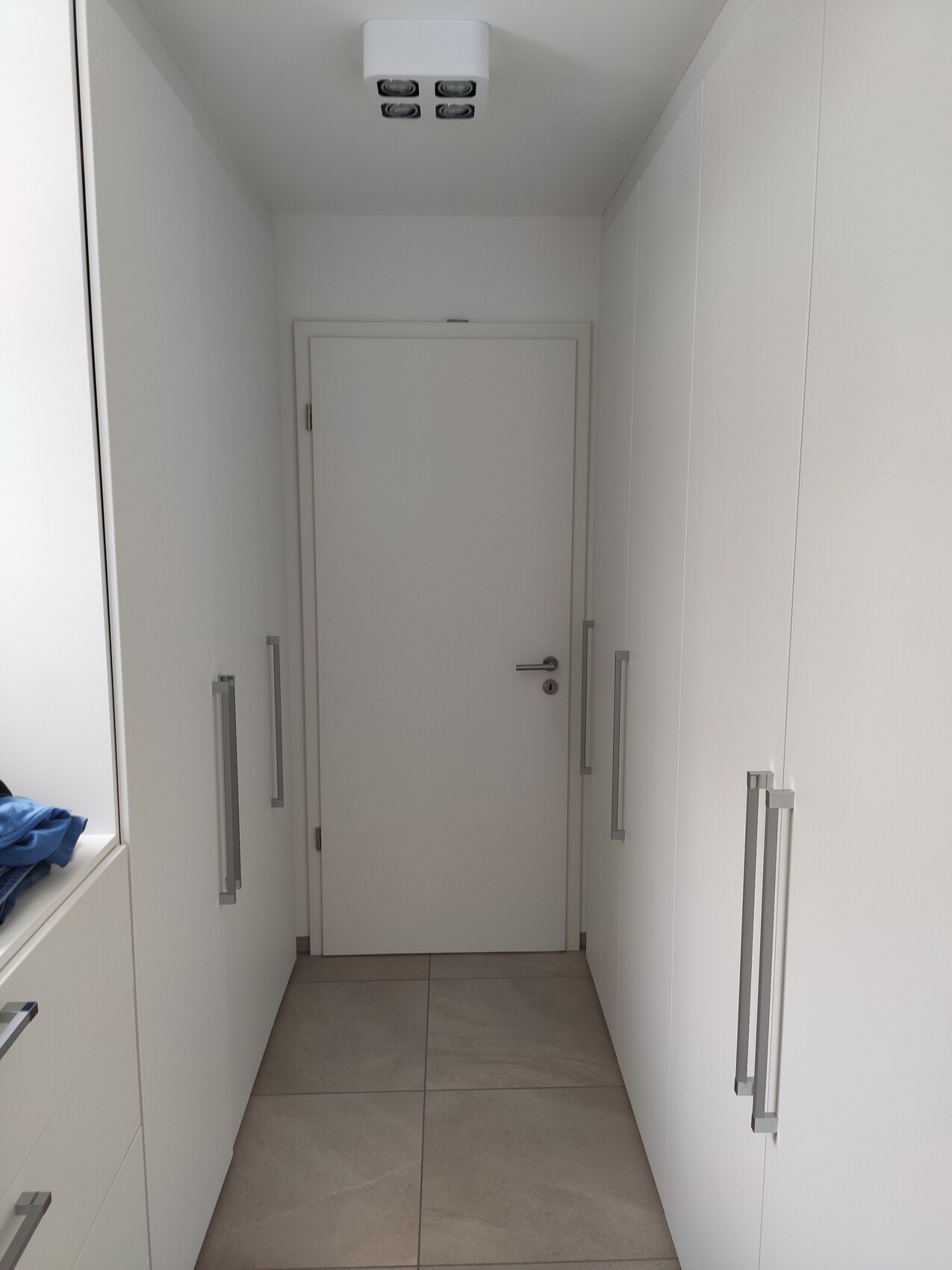 Weißer Flur mit beidseitigen Einbauschränken, Tür am Ende, moderne Deckenleuchte.