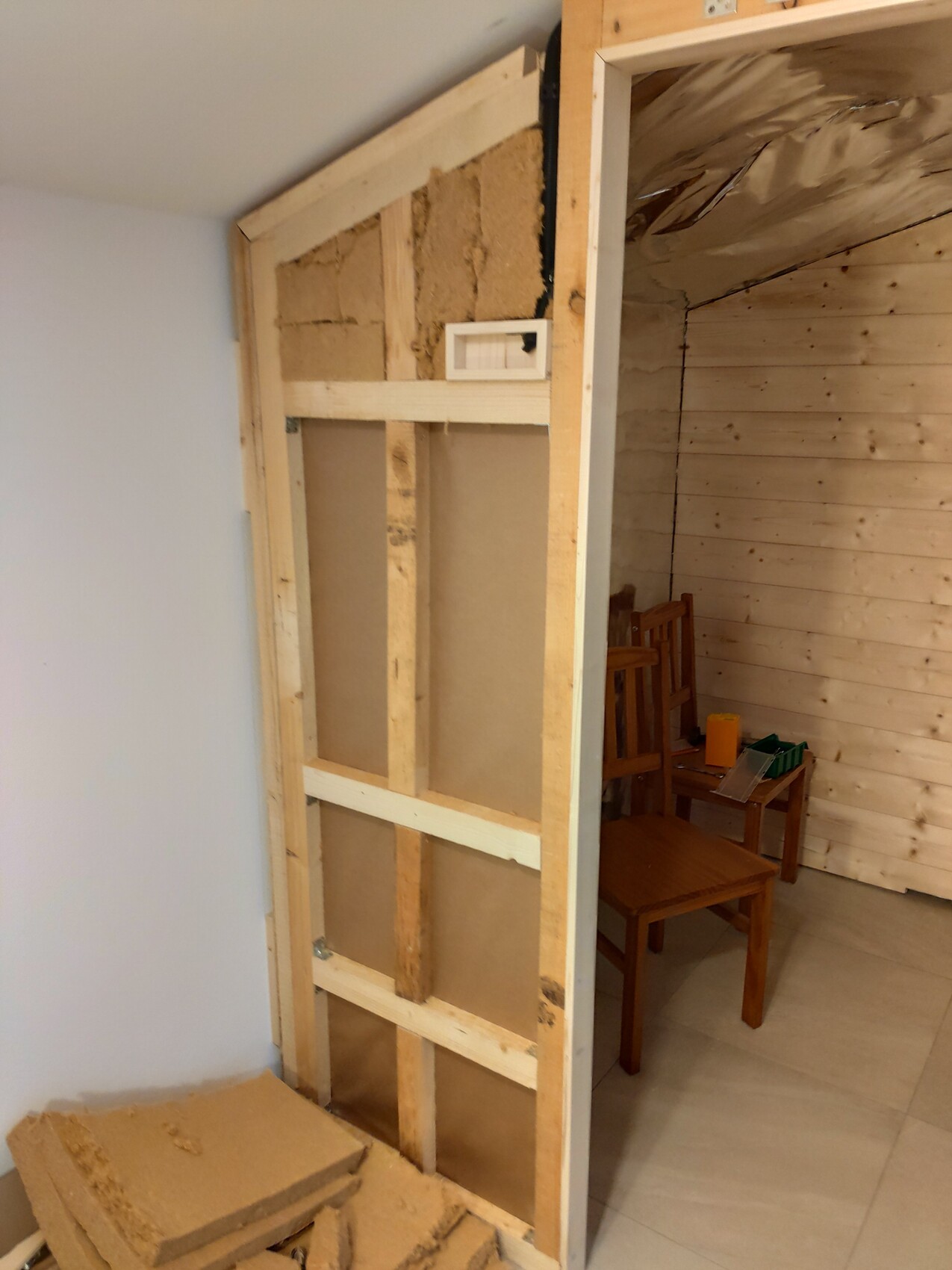 Renovation: exposed stud wall, insulation visible, wooden panels and furniture in the room.
