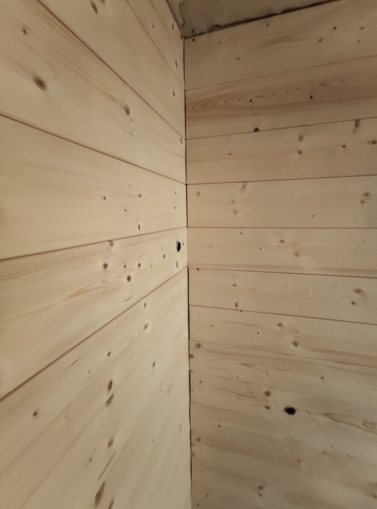 Corner view of a bright wooden wall made of boards with knots and two adjacent wall surfaces.