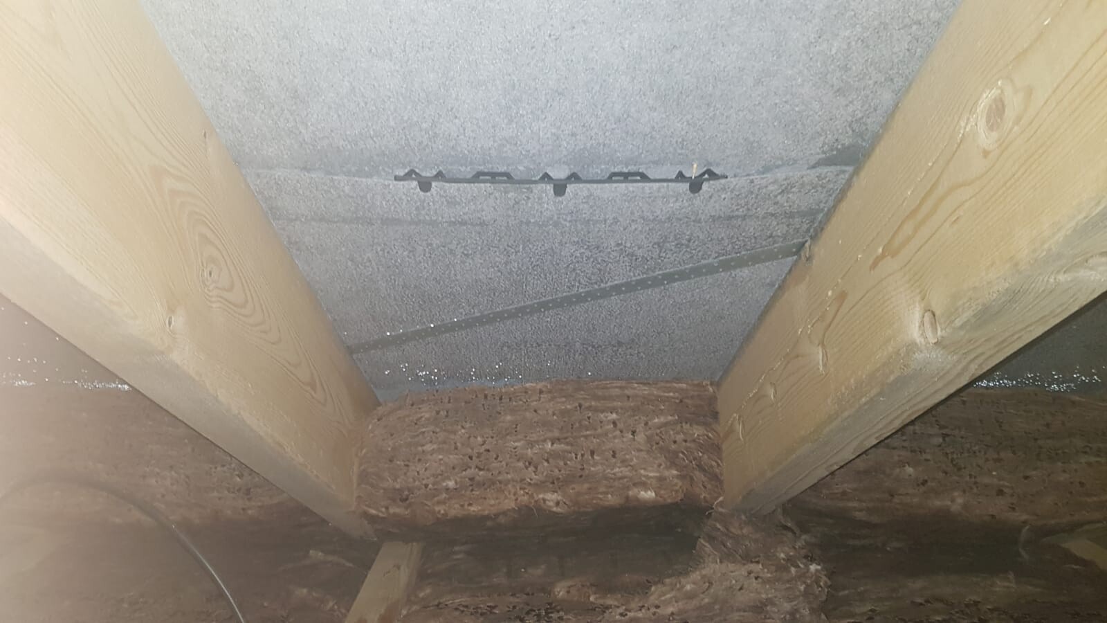 Attic view: two wooden beams, grey ceiling surface, black metal rod with brackets.
