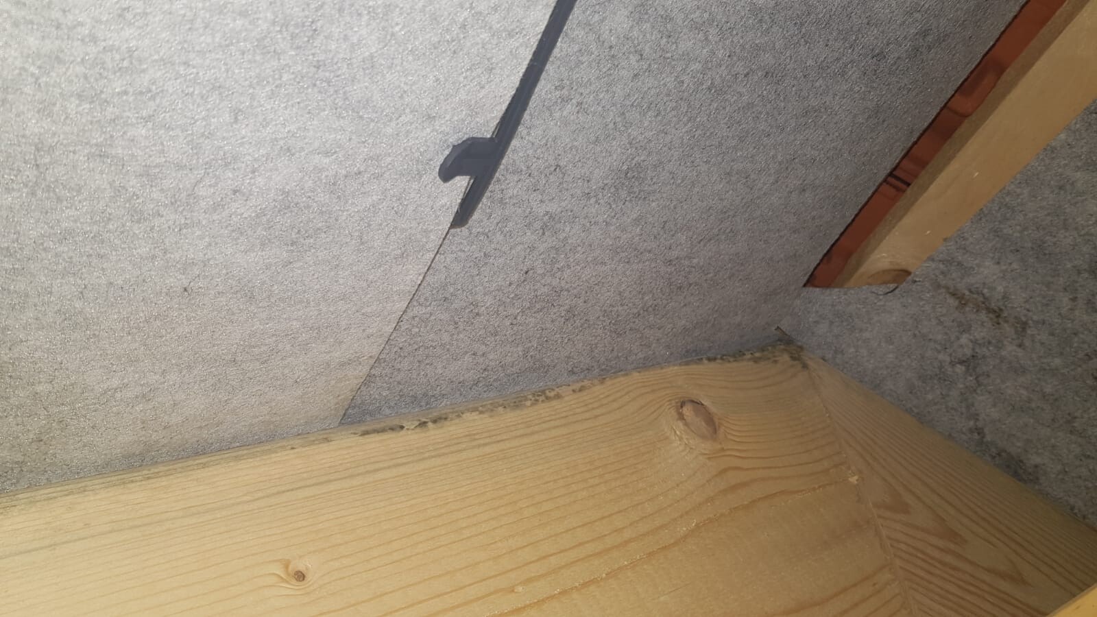 Attic corner with grey insulation board, wooden beam and cable bundle.
