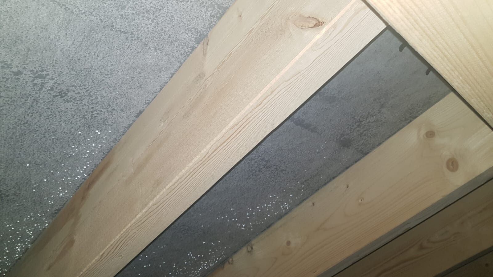 Diagonally arranged wooden beams in front of grey concrete wall; building construction.