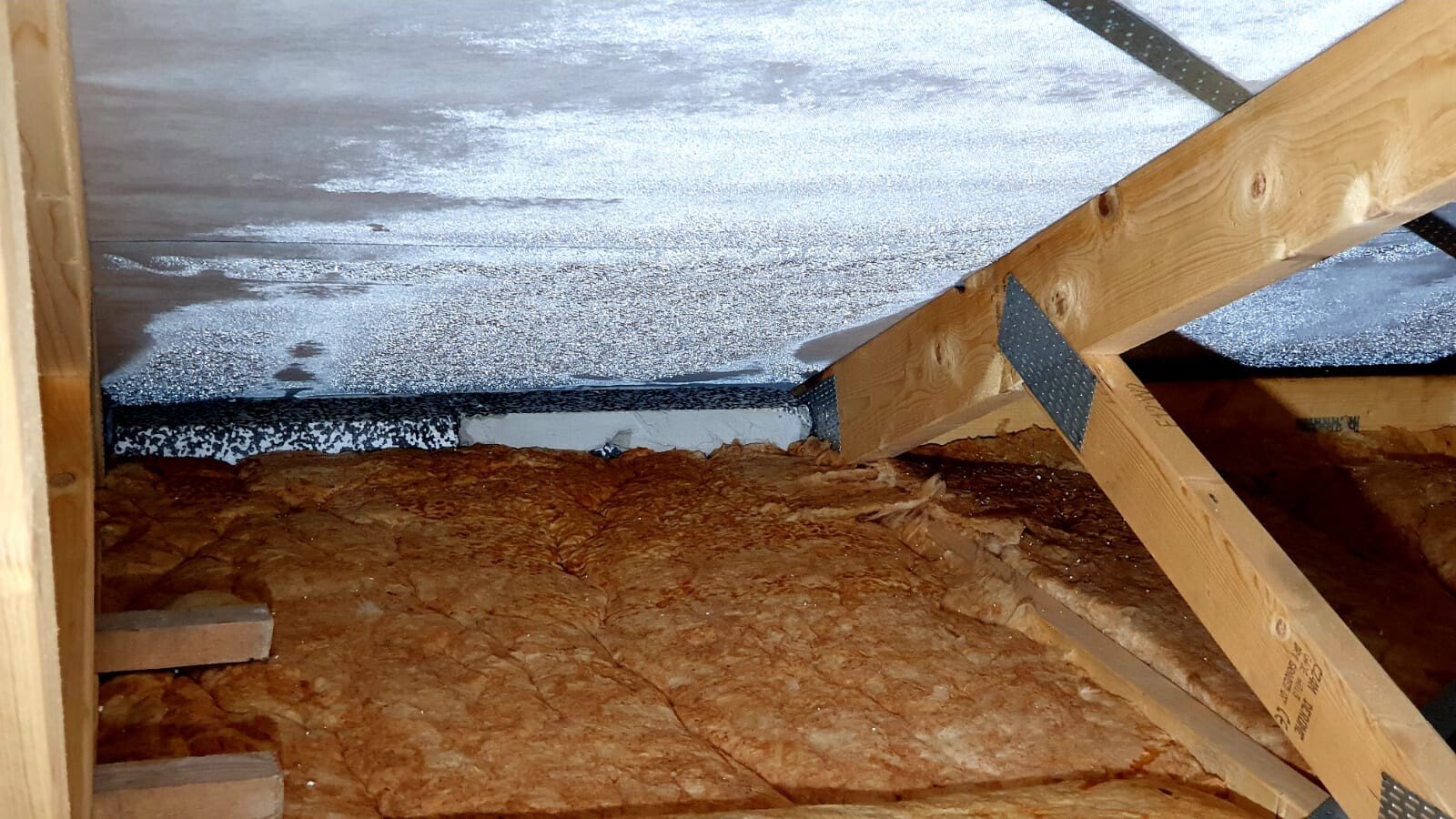Attic with wooden beams, orange mineral wool insulation and reflective roofing membrane.