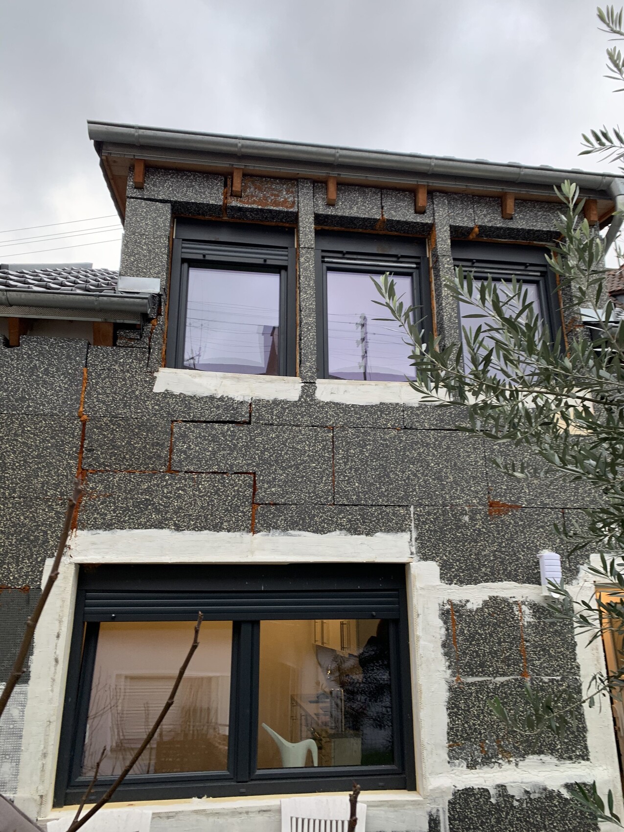 Außenansicht eines Hauses mit großen Fenstern und sichtbarer Baufassade während der Bauphase