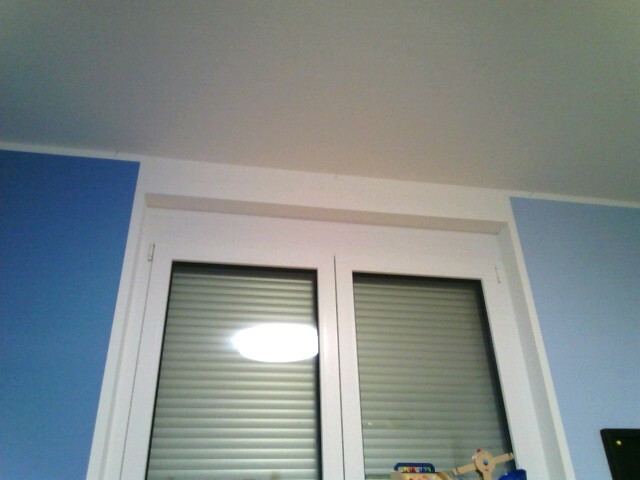 White double window with closed shutters, light blue walls in the room.