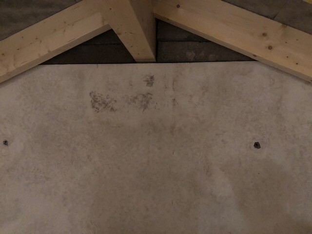 Attic with visible wooden beams and rough concrete/plaster wall in the background.