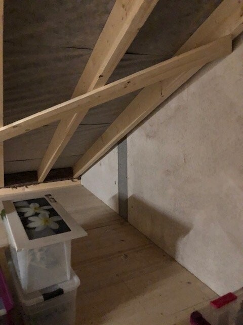 Attic with wooden beams, plastic boxes and a picture frame with white flowers.
