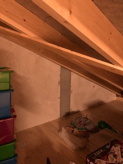 Attic with sloped wooden beam roof, colorful plastic storage boxes on the left, floor with papers and cardboard boxes.