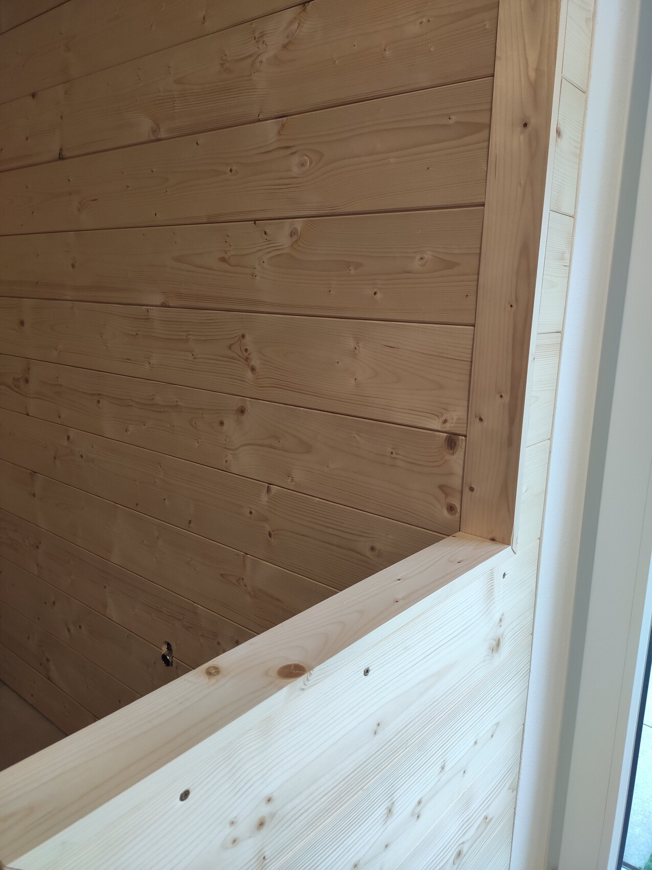 Bright interior with wooden wall of horizontal boards and visible window frame on the right.