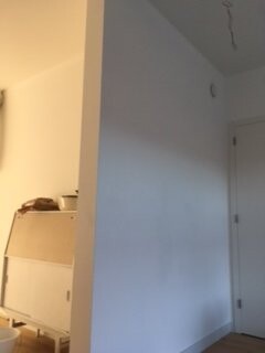 Bright entry area with white wall, door on the right and built-in shelves on the left.