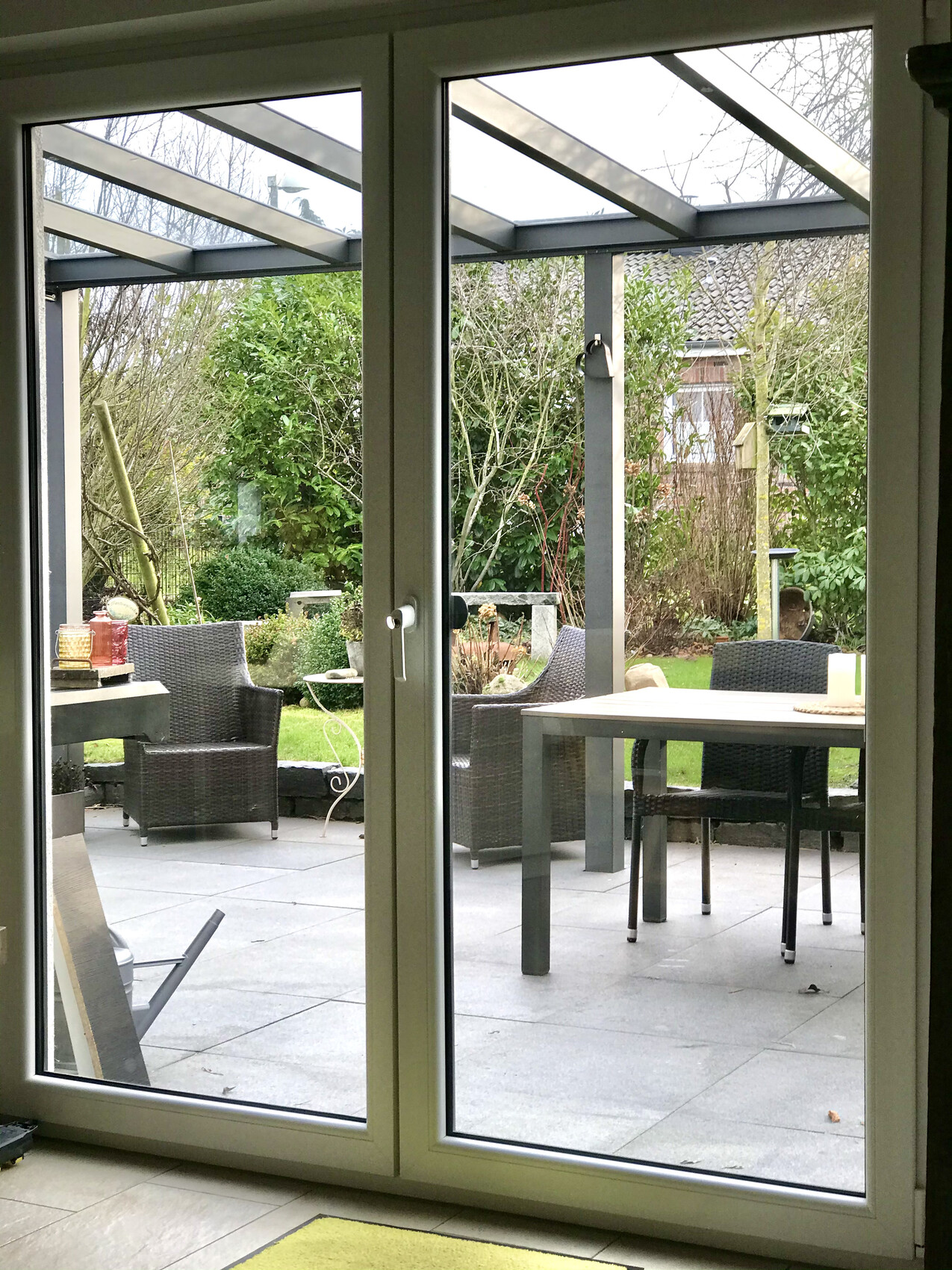 View through glass sliding door onto terrace with dining table and wicker chairs in the garden