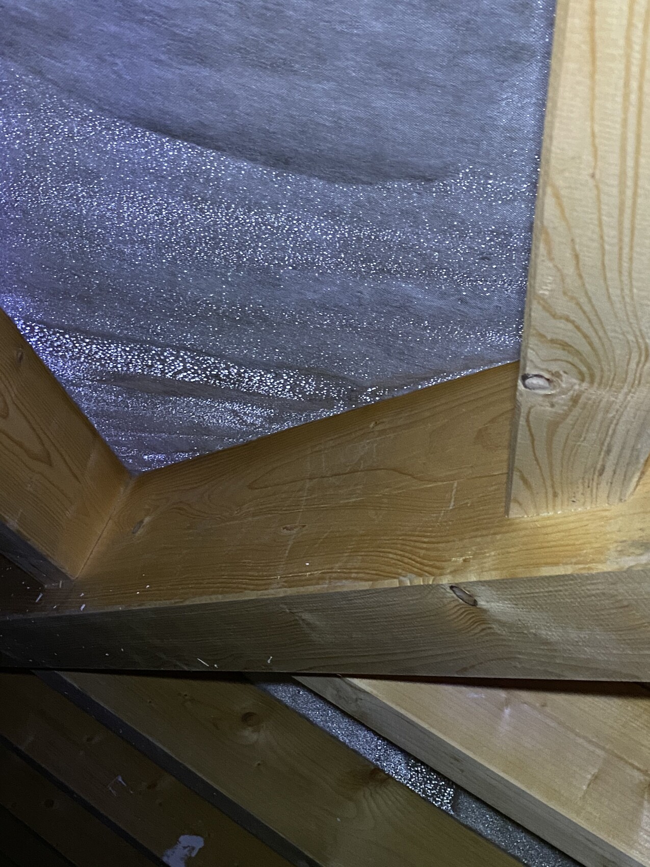 Attic with wooden battens and blue sparkling insulation material between beams.