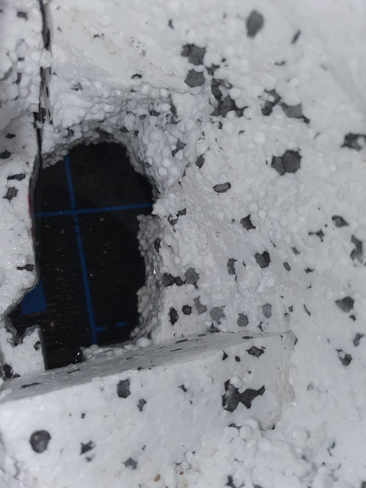 White spray foam around a dark, round hole; blue cross lines visible.